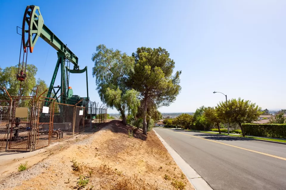 Green oil well behind a fence next to a small street in California.